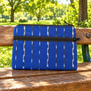A blue solar-panel-patterned zipper pouch with black and white vertical stripes, laid flat on green grass.